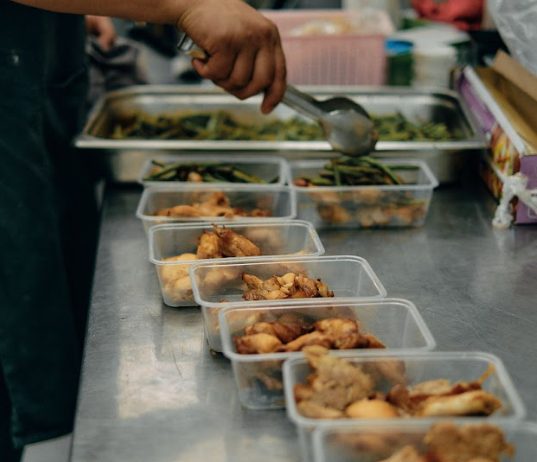 Hands portioning lunch into boxes on a steel counter