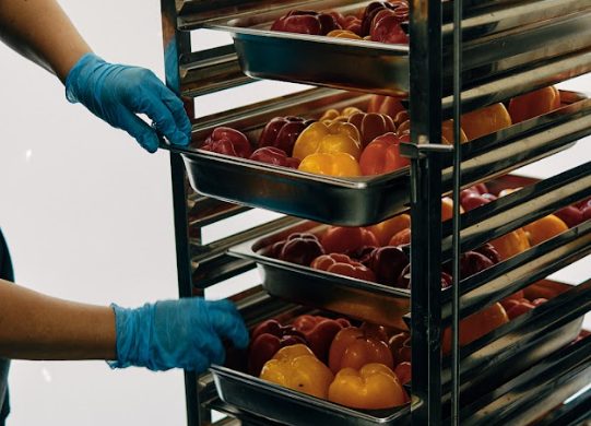 Gloved hands loading a rack of fresh fruit